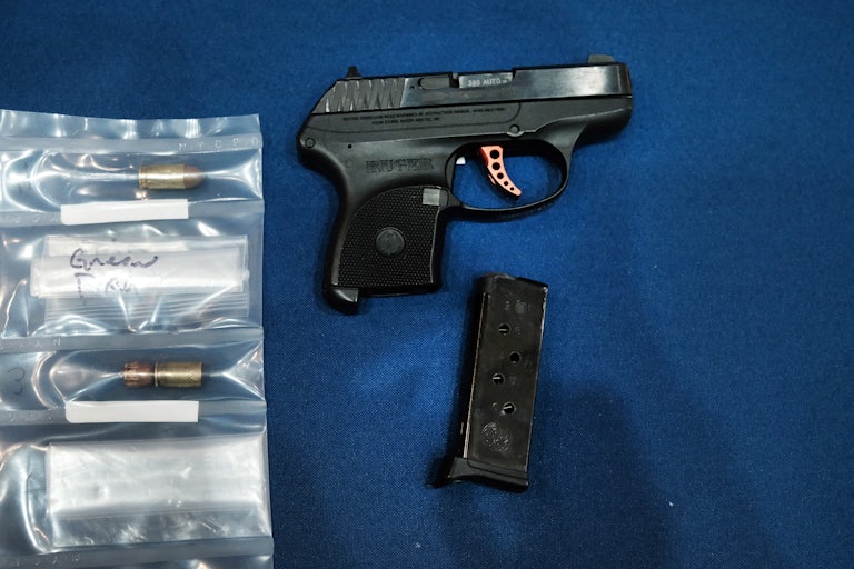 A gun on a table (bullets in a plastic bag beside it)