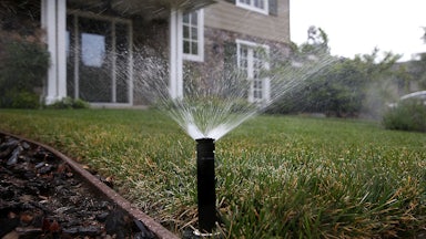 A sprinkler sprays water over a lawn with a house in the background.