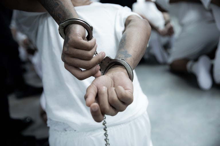 A man with tattoos on his arms has his hands handcuffed behind his back. The photo is of an immigrant deported from the United States to El Salvador’s megaprison.