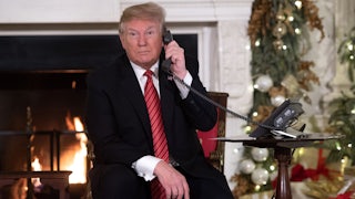 Donald Trump on the phone as he sits in front of the fireplace in a Christmas decorated room.