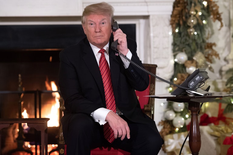 Donald Trump on the phone as he sits in front of the fireplace in a Christmas decorated room.