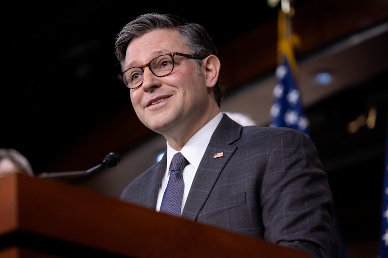 Mike Johnson smiles while speaking at a podium during a press conference