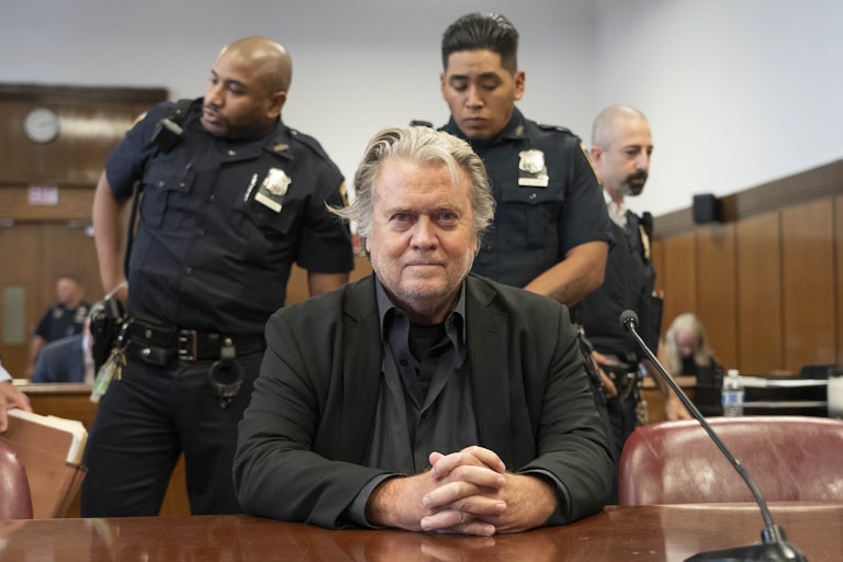 Steve Bannon sits in the courtroom with his hands clasped. Two officers stand behind him.
