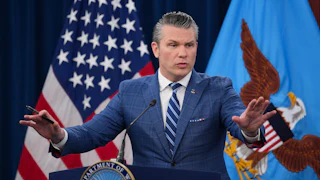 Defense Secretary Pete Hegseth holds both hands out while speaking at a podium