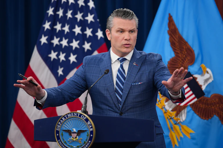 Defense Secretary Pete Hegseth holds both hands out while speaking at a podium