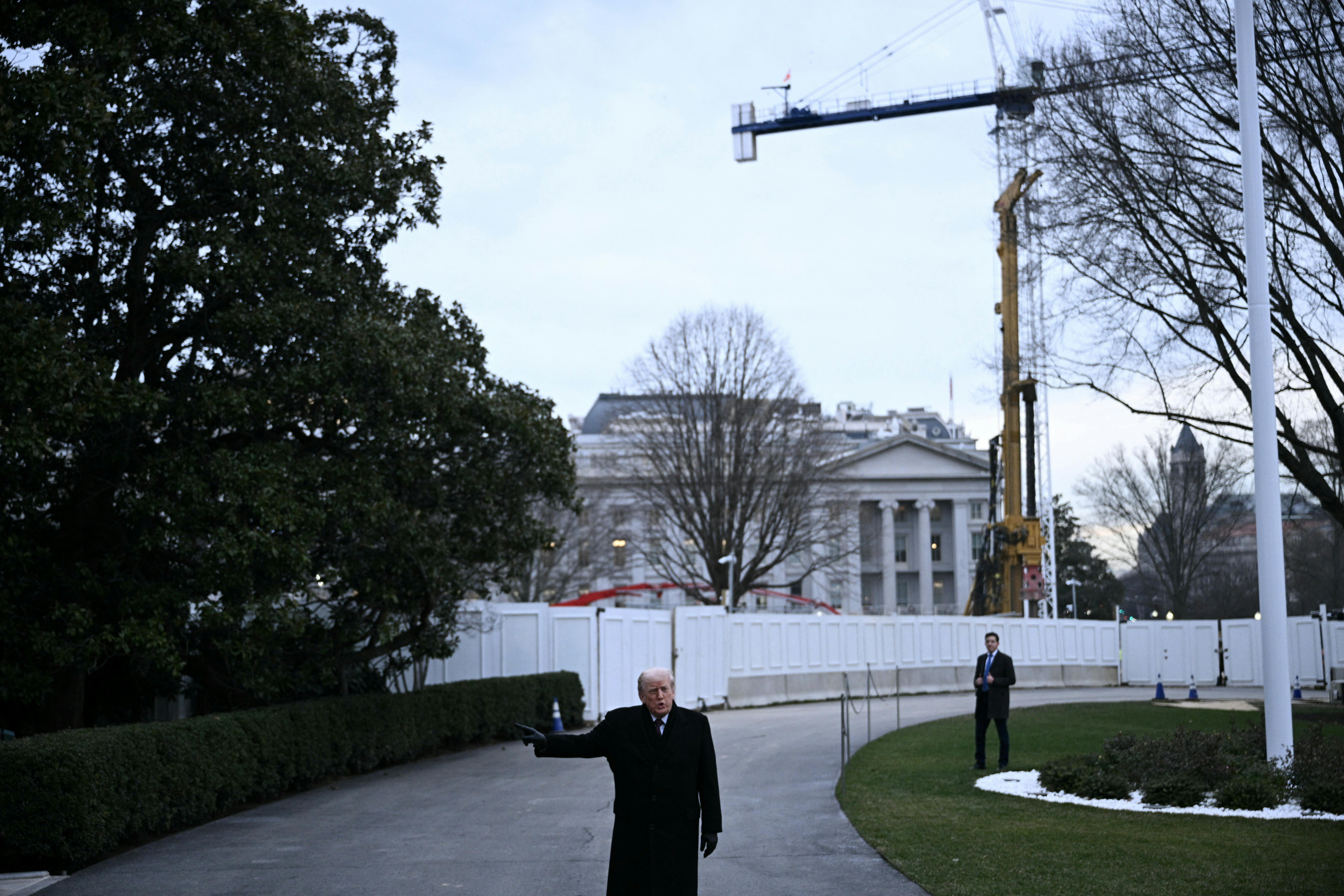 Donald Trump stands in front of the White House as a crane stands overhead.