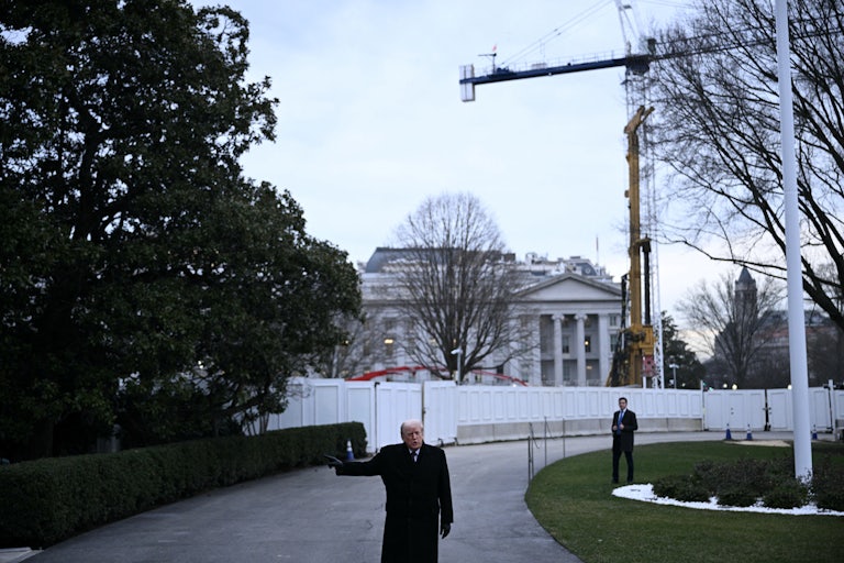 Donald Trump stands in front of the White House as a crane stands overhead.