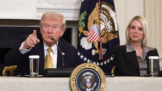 Donald Trump points as Attorney General Pam Bondi smiles. Both are seated a table with the presidential seal.