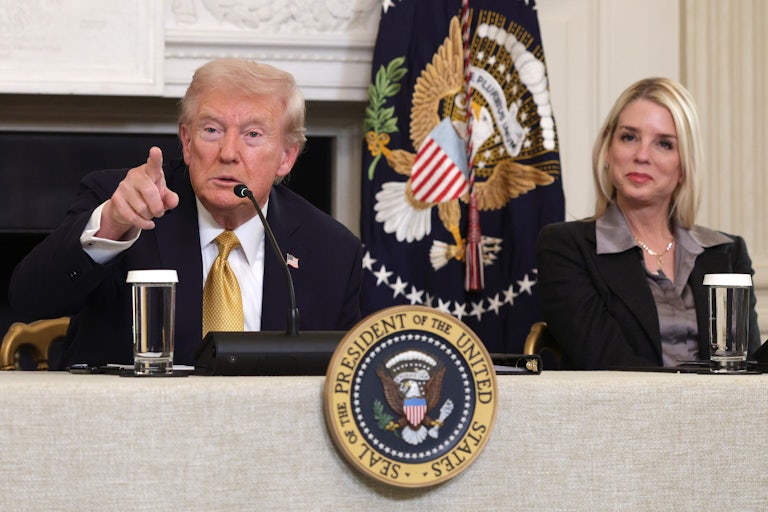 Donald Trump points as Attorney General Pam Bondi smiles. Both are seated a table with the presidential seal.