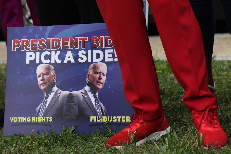 A man in red slacks stands next to a sign urging President Joe Biden to fight for the right to vote.