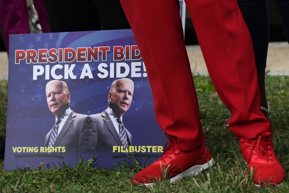 A man in red slacks stands next to a sign urging President Joe Biden to fight for the right to vote.