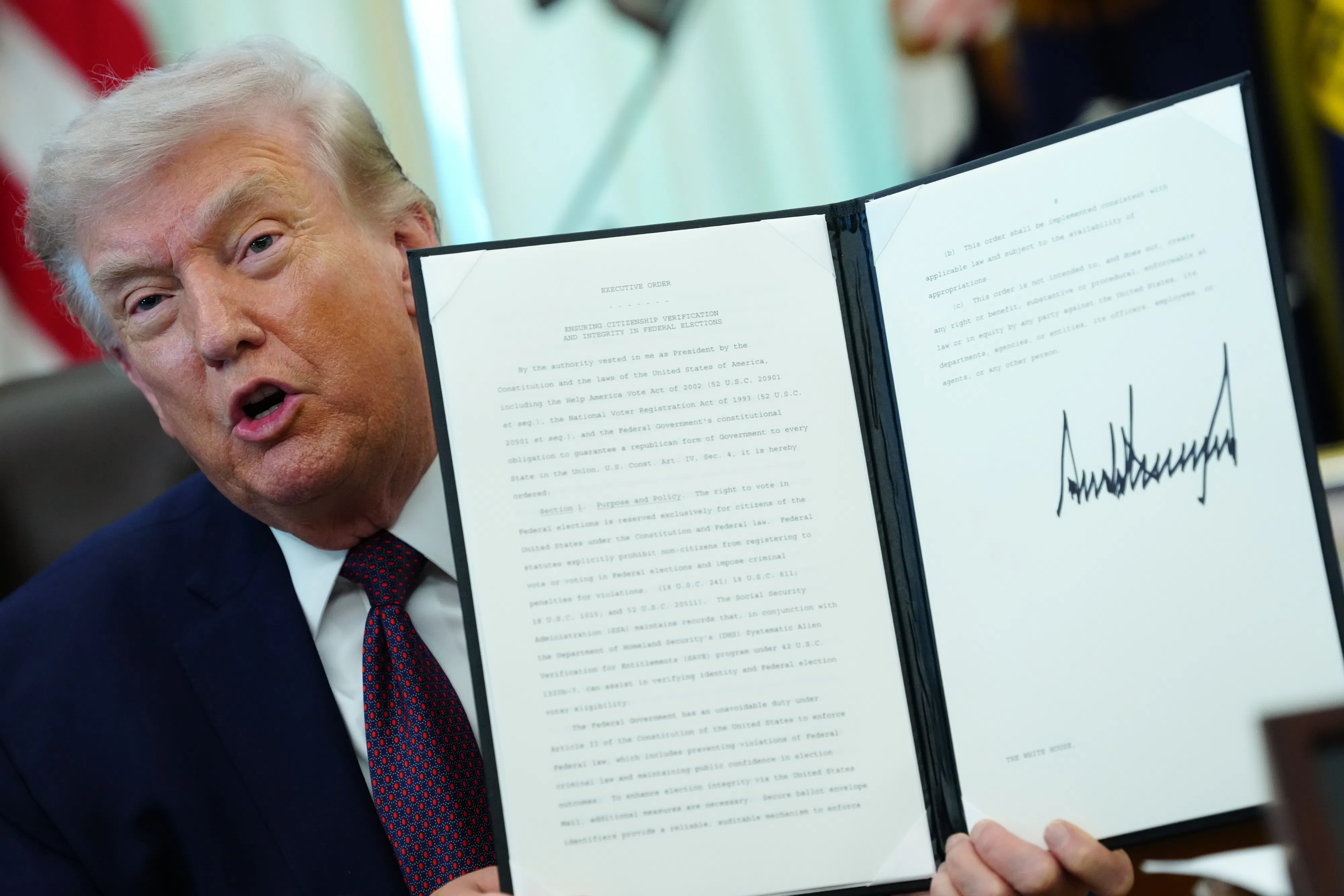Donald Trump holds up a signed executive order and speaks while sitting at his desk in the Oval Office