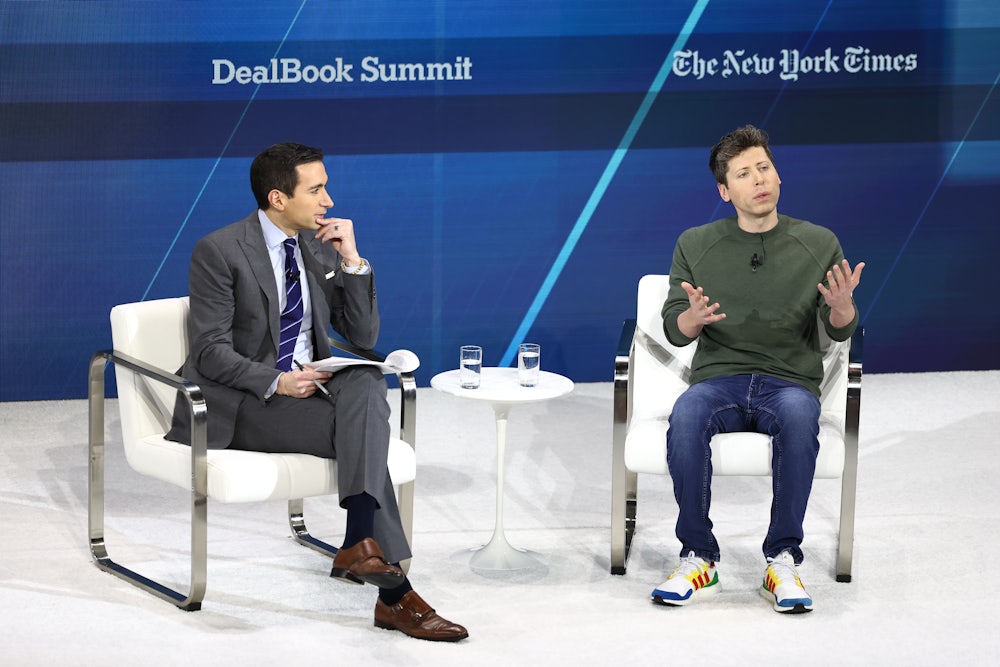 Sorkin, in a suit, sits on a white chair to the left. Altman, in a long-sleeved T-shirt, jeans, and sneakers, sits on a white chair to the right.