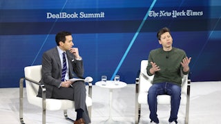 Sorkin, in a suit, sits on a white chair to the left. Altman, in a long-sleeved T-shirt, jeans, and sneakers, sits on a white chair to the right.