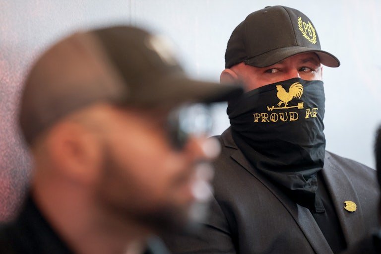 A member of the Proud Boys watches as group leader Enrique Tarrio speaks to reporters