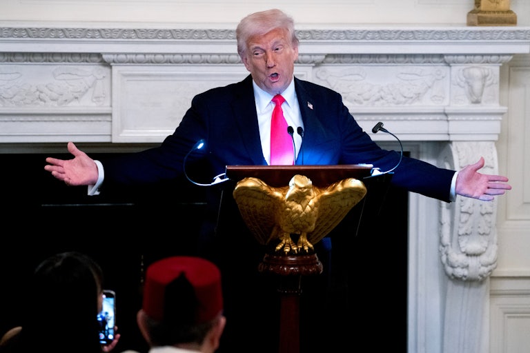 Donald Trump holds his arms out while speaking at a podium in the White House