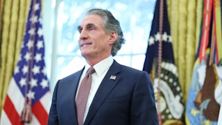 Interior Secretary Doug Burgum folds his hands in front of his stomach and smiles while standing in the Oval Office