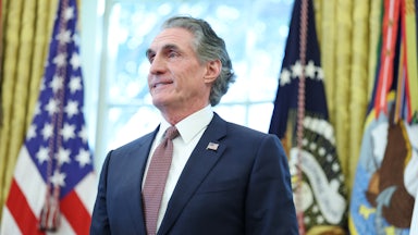 Interior Secretary Doug Burgum folds his hands in front of his stomach and smiles while standing in the Oval Office
