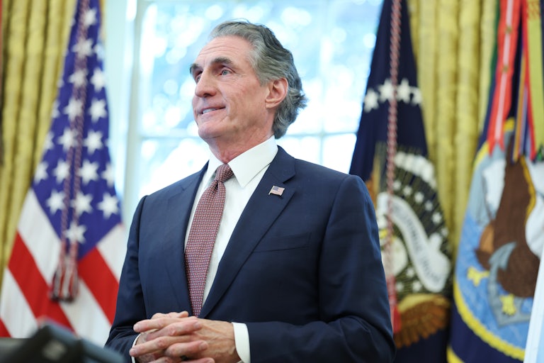 Interior Secretary Doug Burgum folds his hands in front of his stomach and smiles while standing in the Oval Office
