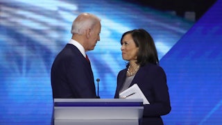 Kamala Harris looks up at Joe Biden and smiles as they stand behind a lectern in 2019
