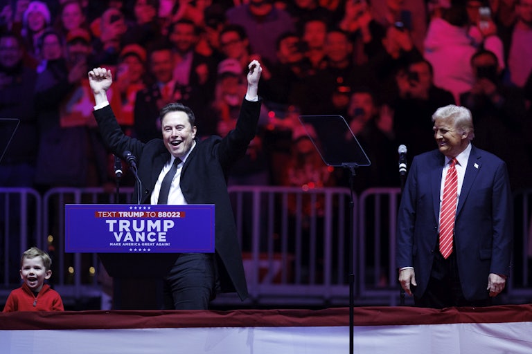 Elon Musk holds his arms above his head while standing at a podium, as Donald Trump smiles and looks on