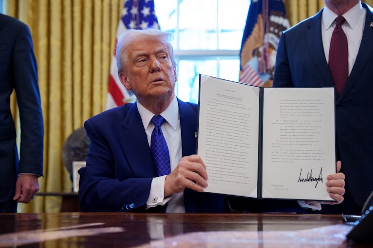 Trump holds up a signed executive order for the cameras (not pictured) while he sits at his desk in the Oval Office.