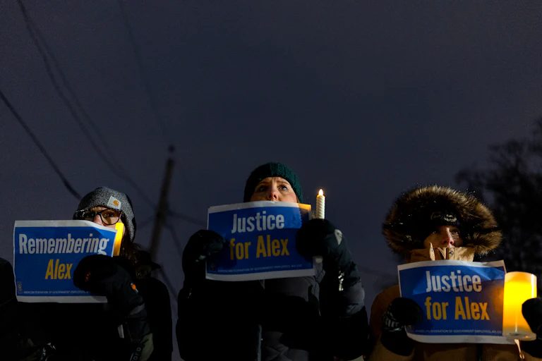 Three people hold up signs in memory of Alex Pretti during a vigil for him in Minneapolis, Minnesota