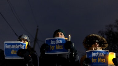 Three people hold up signs in memory of Alex Pretti during a vigil for him in Minneapolis, Minnesota