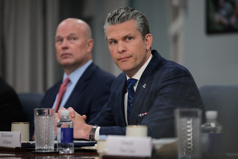 Pete Hegseth listens in a meeting, with his hands clasped on a table.