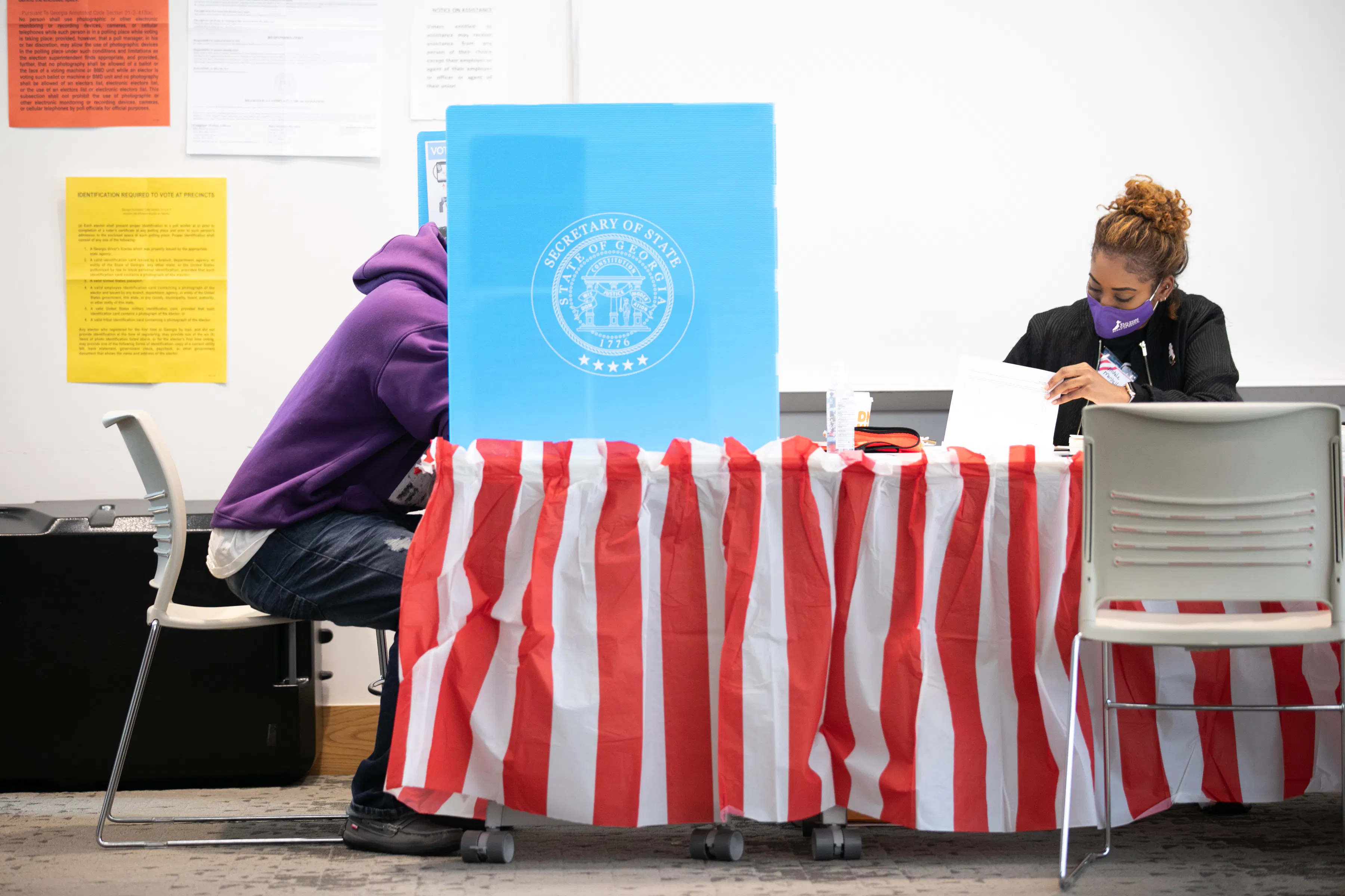 Sitting next to a masked poll worker, a Fulton County voter casts a ballot.