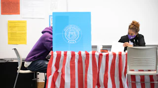 Sitting next to a masked poll worker, a Fulton County voter casts a ballot.