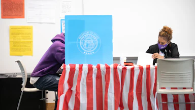Sitting next to a masked poll worker, a Fulton County voter casts a ballot.
