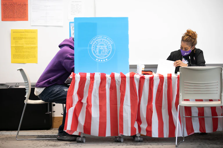 Sitting next to a masked poll worker, a Fulton County voter casts a ballot.