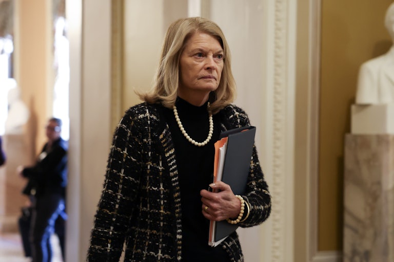 Senator Lisa Murkowski holds a binder and walks in the Capitol