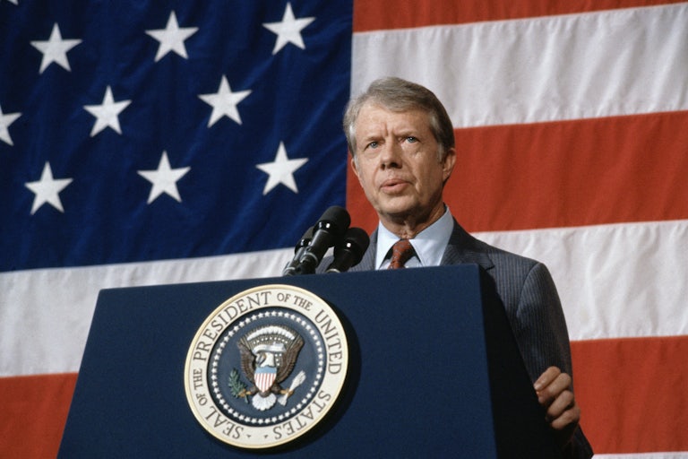 Jimmy Carter stands at a podium in front of an American flag.