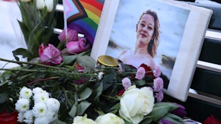 Standing outside in the dark, multiple people hold up a large poster reading "Fucking Bitch."