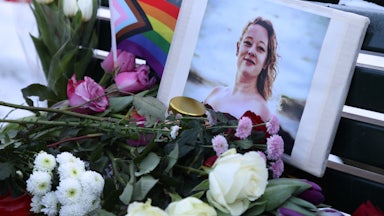 Standing outside in the dark, multiple people hold up a large poster reading "Fucking Bitch."
