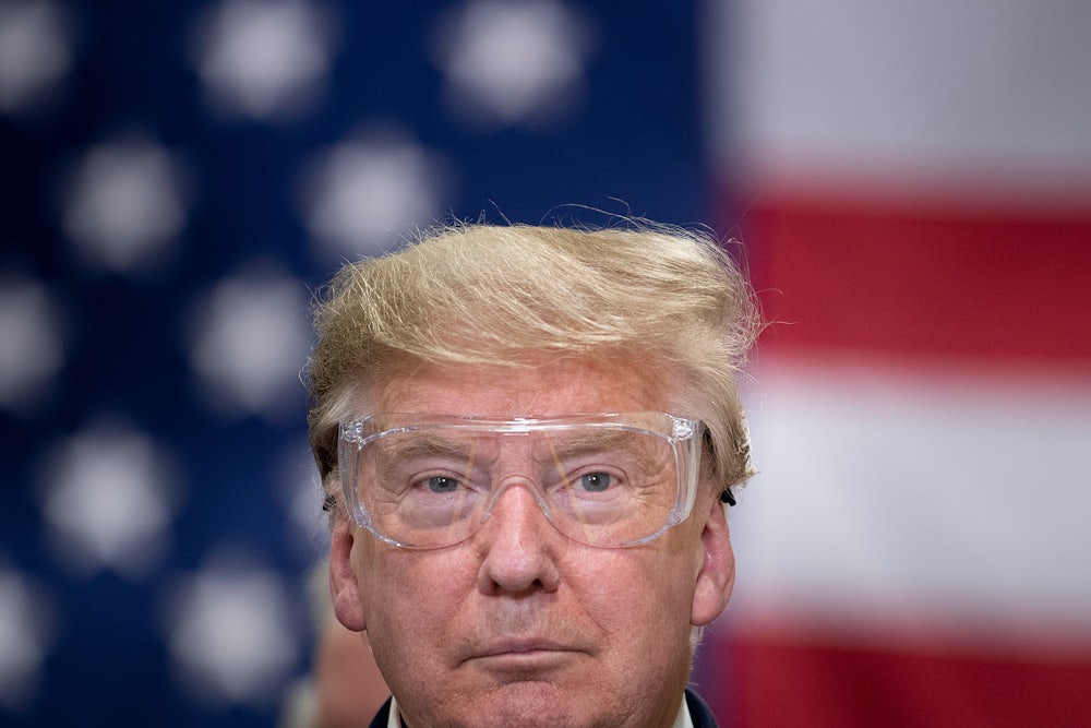 Donald Trump wears safety glasses while standing in front of an American flag.