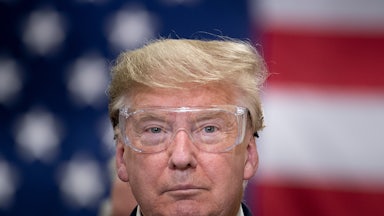 Donald Trump wears safety glasses while standing in front of an American flag.