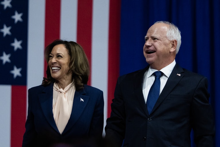 Kamala Harris and Tim Walz smile as they stand next to each other at their first joint rally