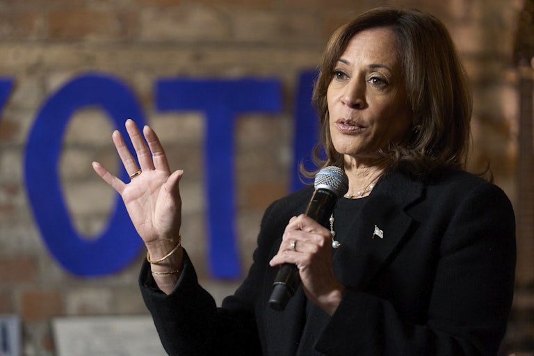 Kamala Harris gestures and holds up a microphone while speaking