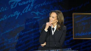Kamala Harris stands behind a podium and holds her chin as she listens to Donald Trump say some crazy shit.