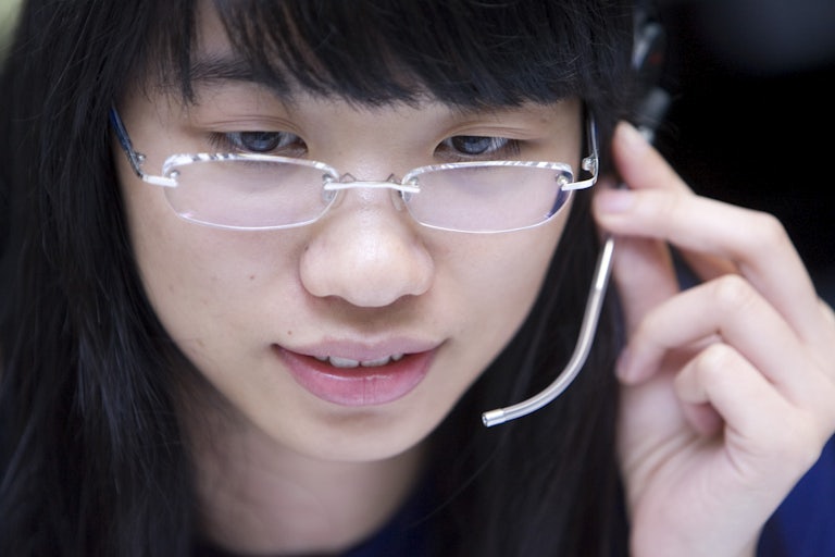 A Chinese woman with glasses speaks into a mic headset.