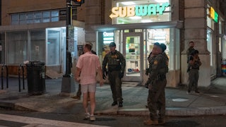 Sean Dunn, wearing a pink polo and shorts, stands outside a Subway along with seven federal agents.