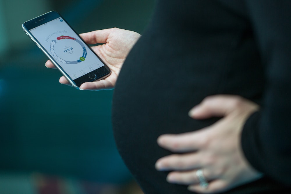 A pregnant woman holds a cell phone displaying a screen from the Clue health app.
