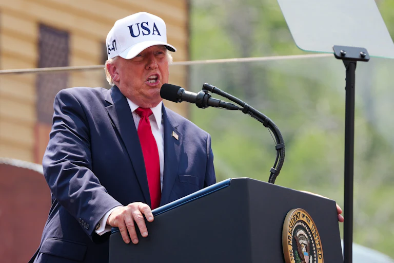 Donald Trump yelling at a podium while wearing a white USA cap