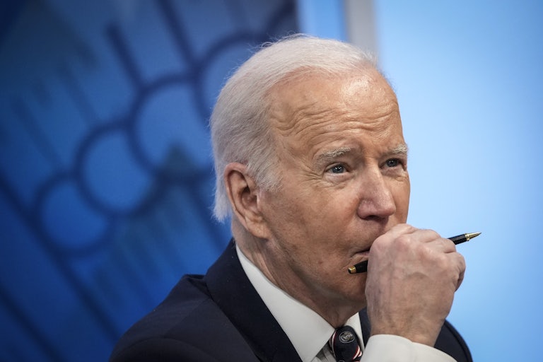 A close up of a pensive President Joe Biden, holding a pen in front of his face.