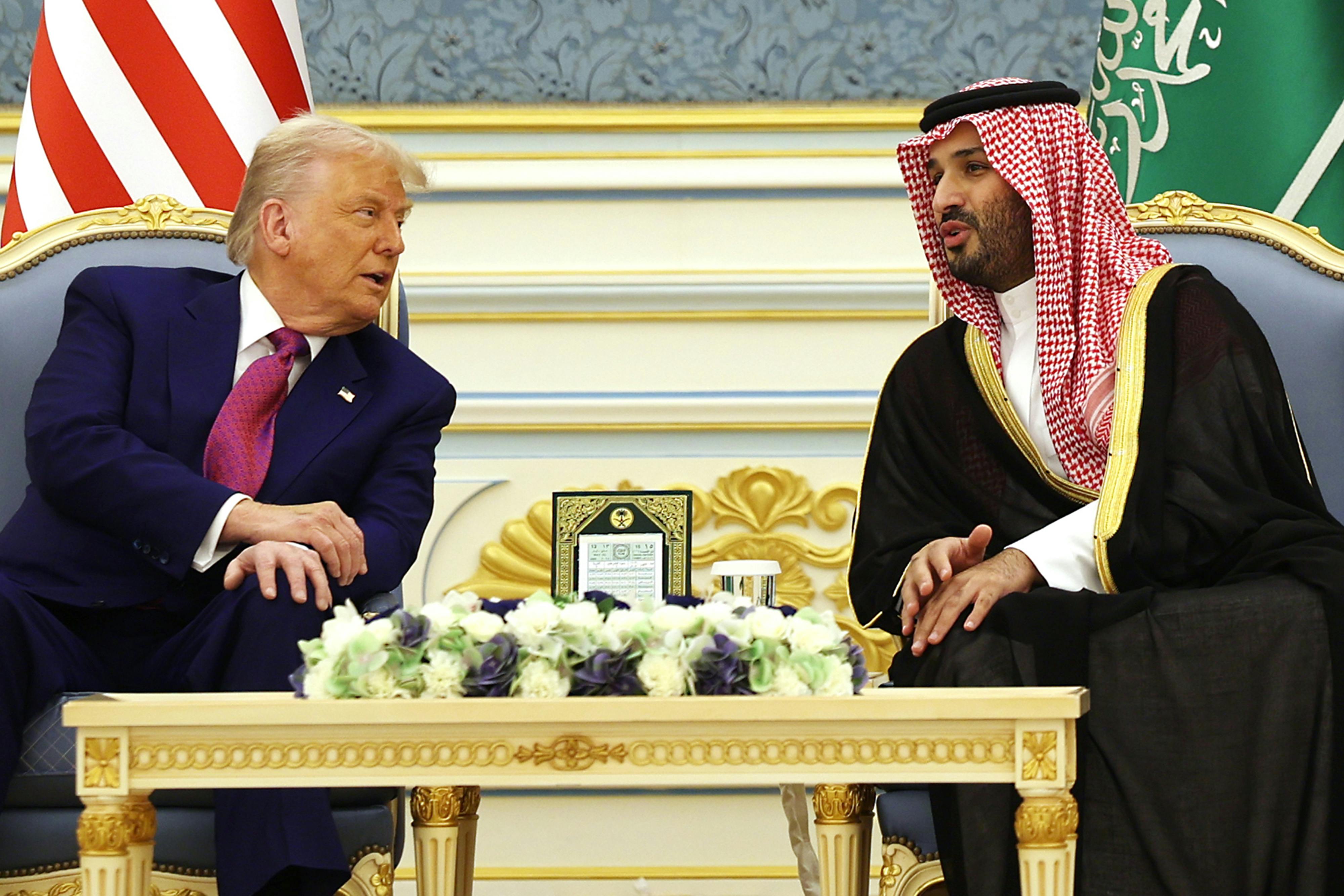 Donald Trump and Saudi Crown Prince Mohammed bin Salman lean over to speak to each other while seated with a table between them.