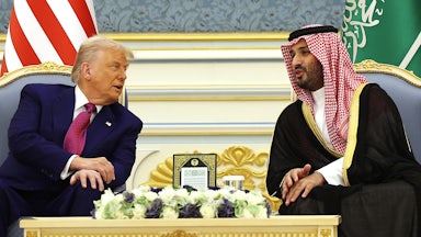 Donald Trump and Saudi Crown Prince Mohammed bin Salman lean over to speak to each other while seated with a table between them.