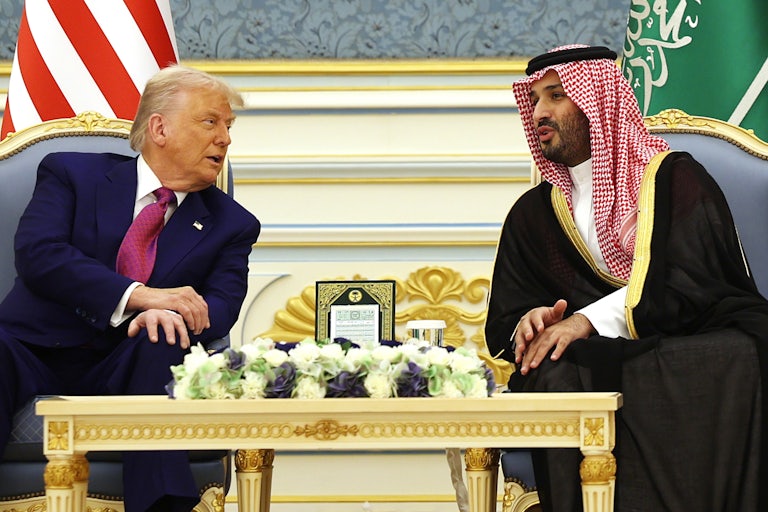 Donald Trump and Saudi Crown Prince Mohammed bin Salman lean over to speak to each other while seated with a table between them.